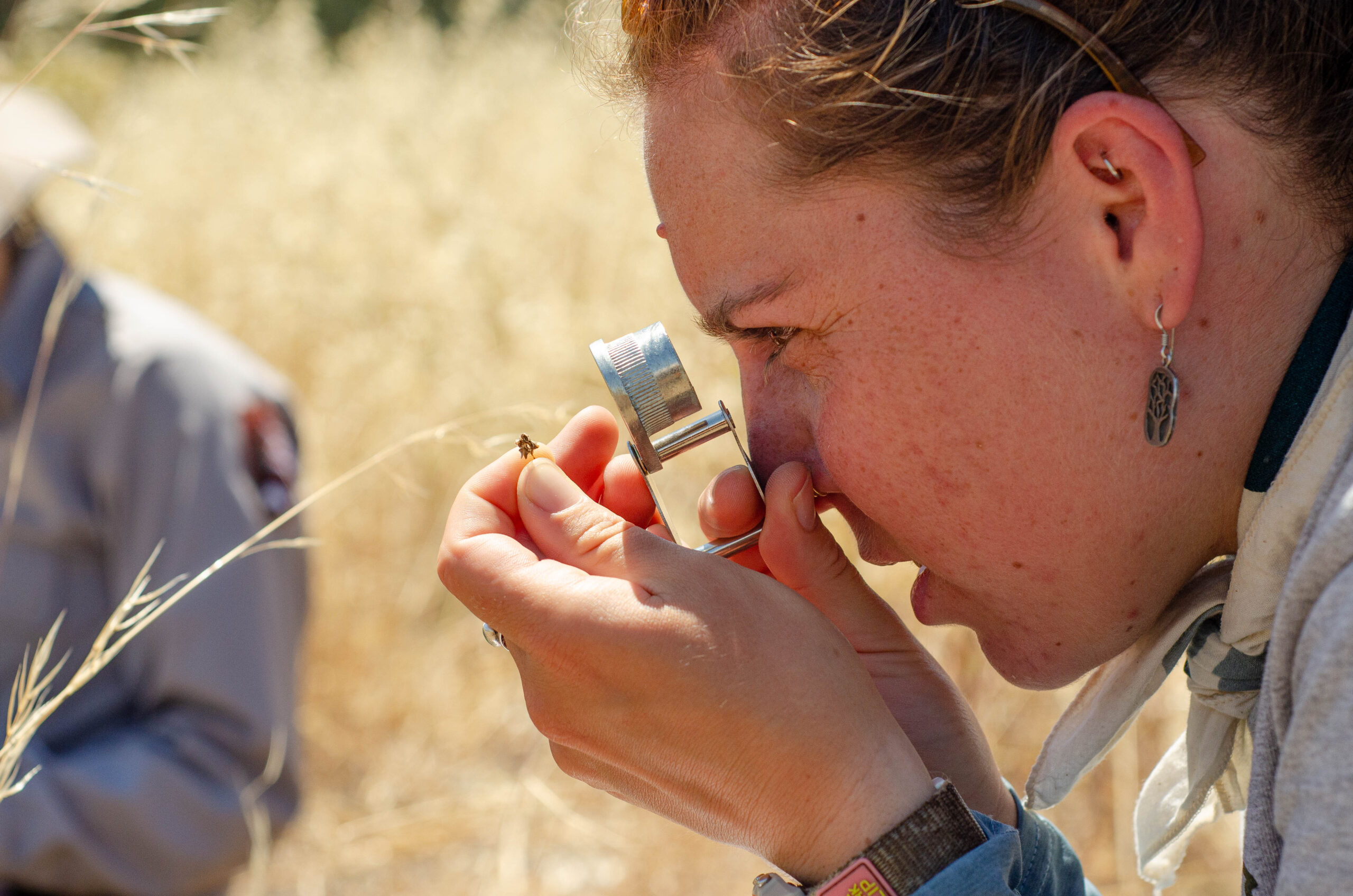 A close-up of a woman looking at a seed through a hand lens.