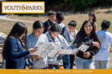 A group of youth outside looking at bird guides and laughing.