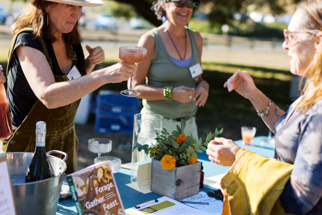 A woman passes a cocktail to a customer, laughing.