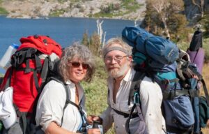 Two people wearing large backpacks posing in front of a lake