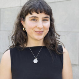 A woman with brown hair and wearing a black shirt smiles brightly at the camera.