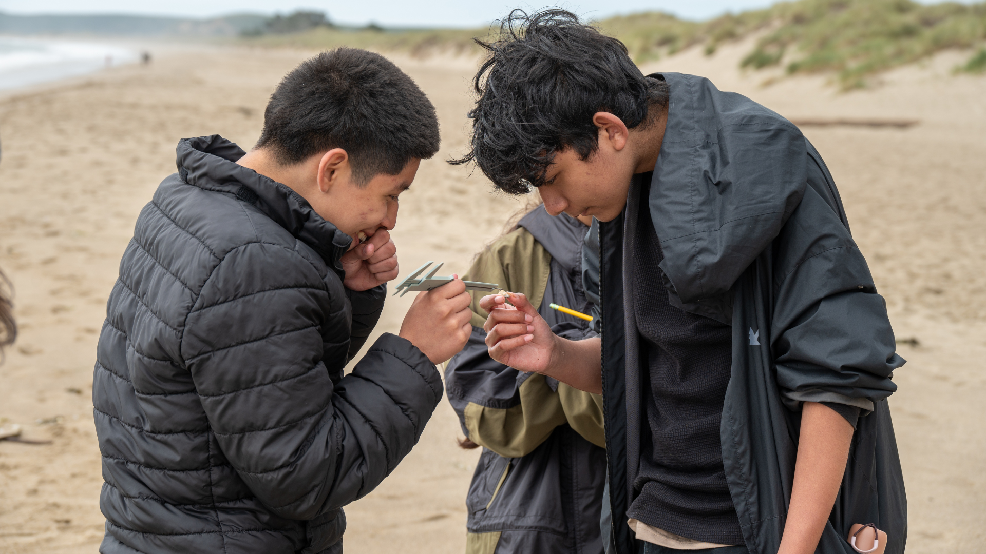 Two people with black jackets look closely at a ruler.